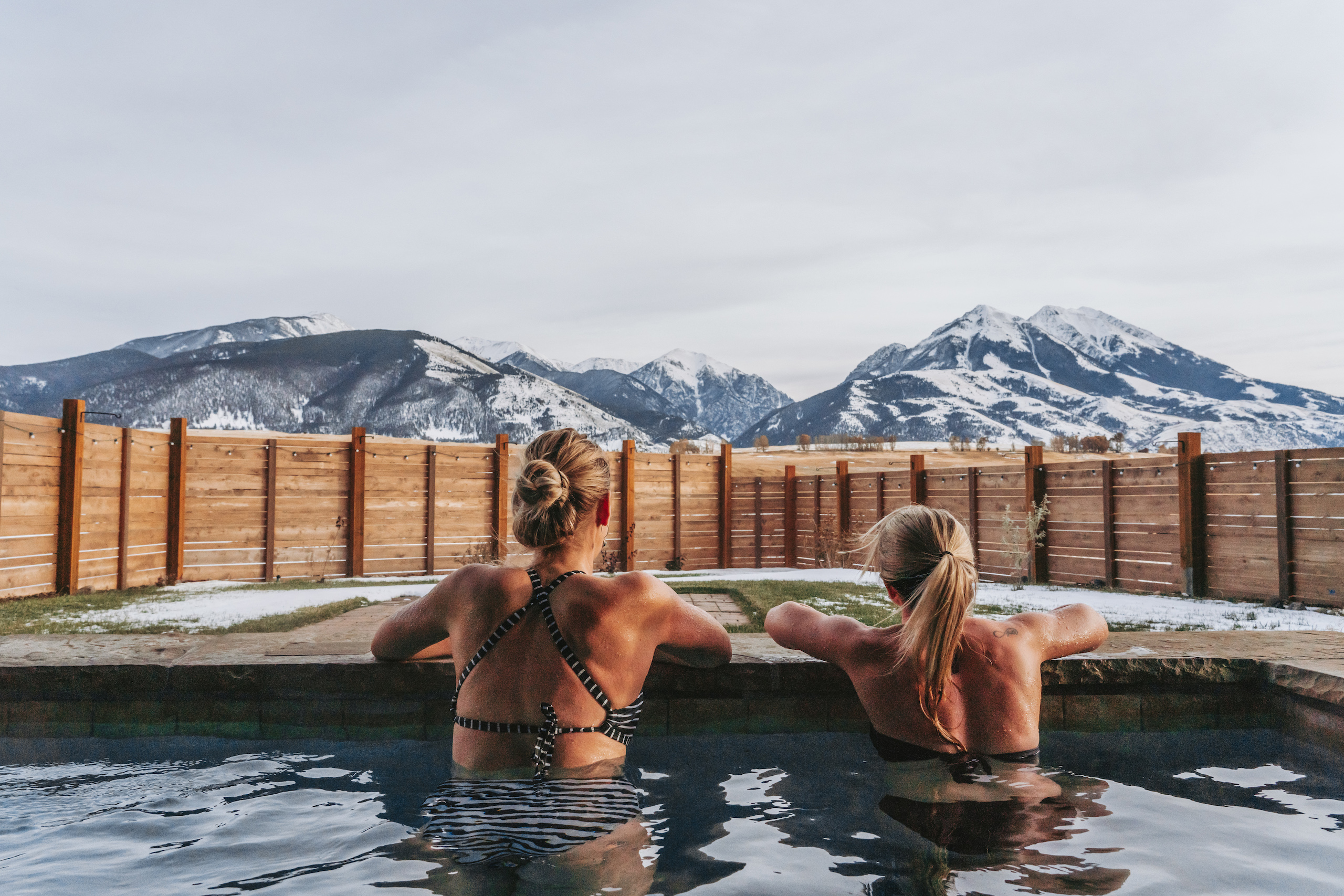 Two women in a hot tub looking out at snowy mountains