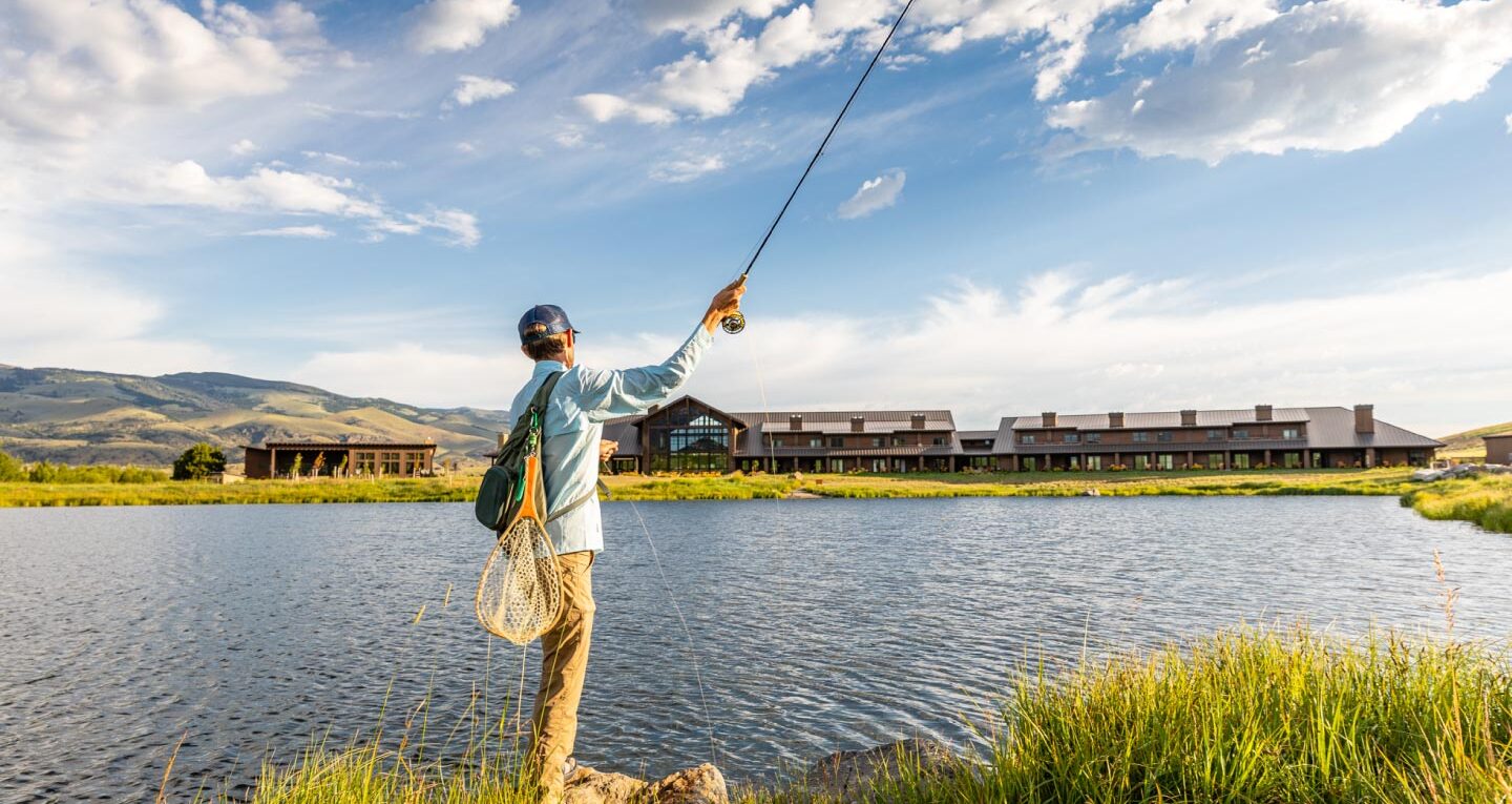 man flyfishing on lake in front of lodge